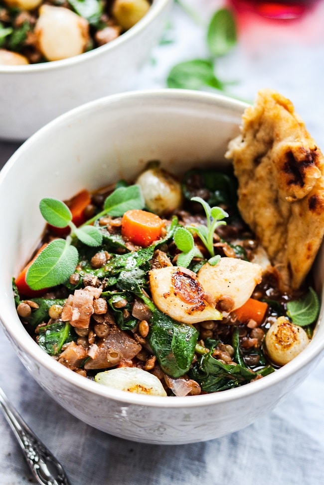 Red Wine Braised Lentils with Spinach and Pearl Onions served in a white bowl with naan.