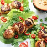 Seared scallops wrapped in bibb lettuce leaves and garnished with sliced fresno peppers.