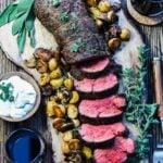 Roasted beef tenderloin served on rustic wooden board and red wine on the side.