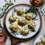 French onion smashed potatoes on a white plate and topped with fresh herbs and beer on the side.