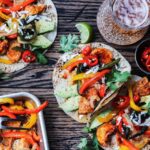 Mexican chicken fajitas served straight from sheet pan onto warmed tortillas with sliced avocado on wooden surface.