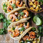 Air fryer shrimp tacos topped with pineapple salsa, cilantro and crema on a wooden board.
