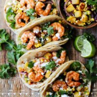 Air fryer shrimp tacos topped with pineapple salsa, cilantro and crema on a wooden board.