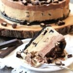Slice of ice cream cake on a white plate with a fork with the rest of the cake in the background.