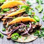 Close up of juicy short rib beef in flour tortillas on a dark wooden surface.