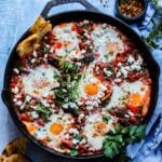Moroccan shakshuka in a large skillet topped with feta, fresh herbs and red pepper flakes.