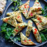 Several triangle-shaped parmesan zucchini bites arranged on a charcoal platter and garnished with fresh herbs.