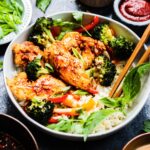Bulgogi chicken over rice in a bowl with broccoli and red peppers. Gochujang and green onions in the background.