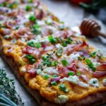 Close up of crispy prosciutto, goat cheese crumbles, sliced green onions and shallots on top of butternut squash flatbread.