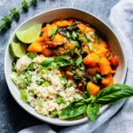 Pumpkin curry served over brown rice in a white bowl with a blue linen napkin on the right side.