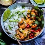 Thai red shrimp curry on one side of white bowl with jasmine rice on the other half, topped with green onion slices.