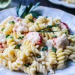 Close up of creamy seafood mac n cheese garnished with parsley and chopped chives on an off-white plate.