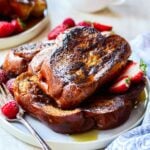 Close up of french toast on a white plate with a fork and raspberries on the side.