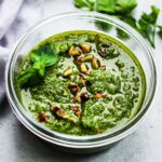 Spinach walnut pesto topped with chopped walnuts and fresh basil in a glass bowl on a white surface.